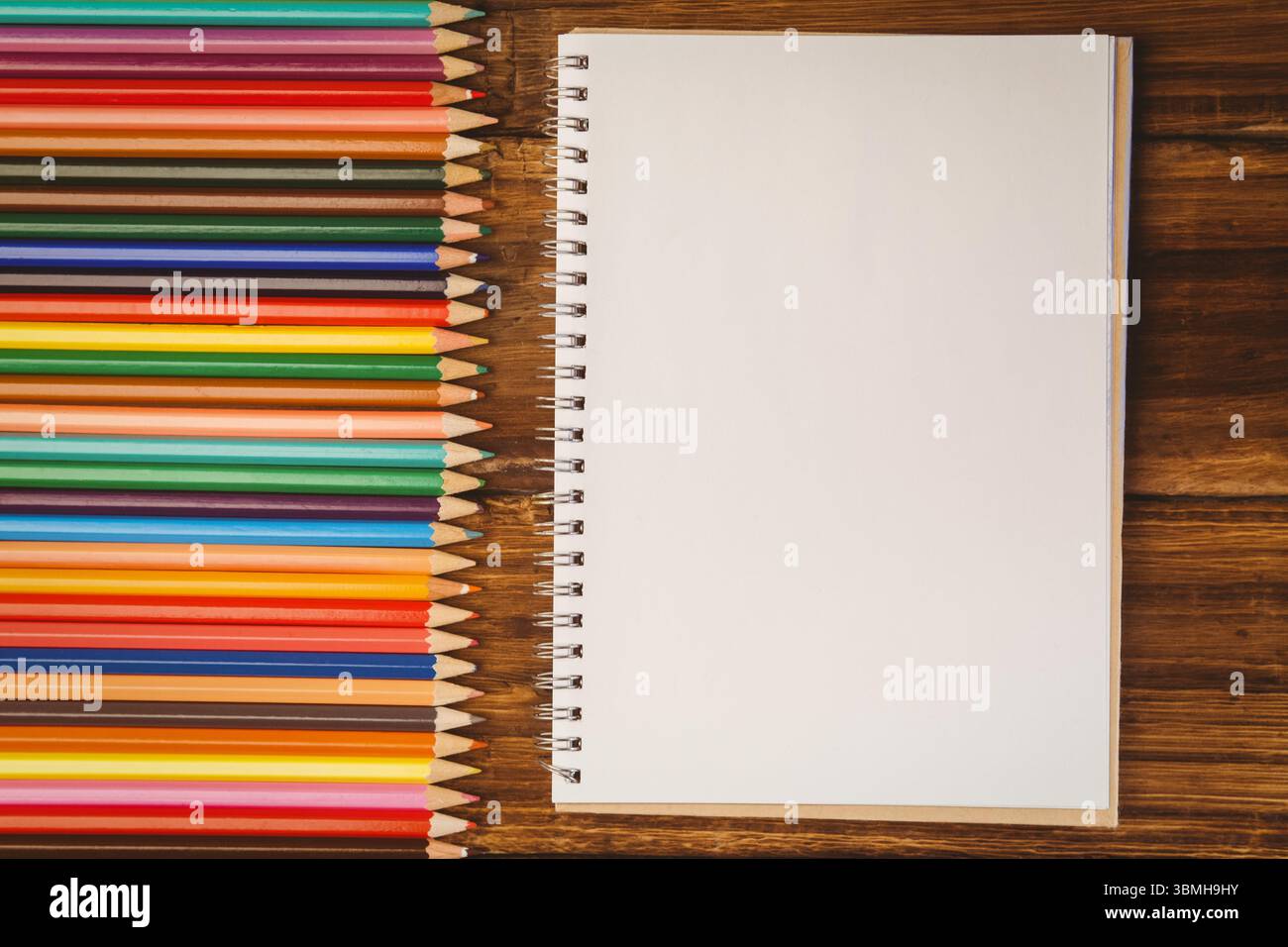 Flat lay illustration is showing spiral-bound notebook with colored pencils on wooden desk Stock Photo