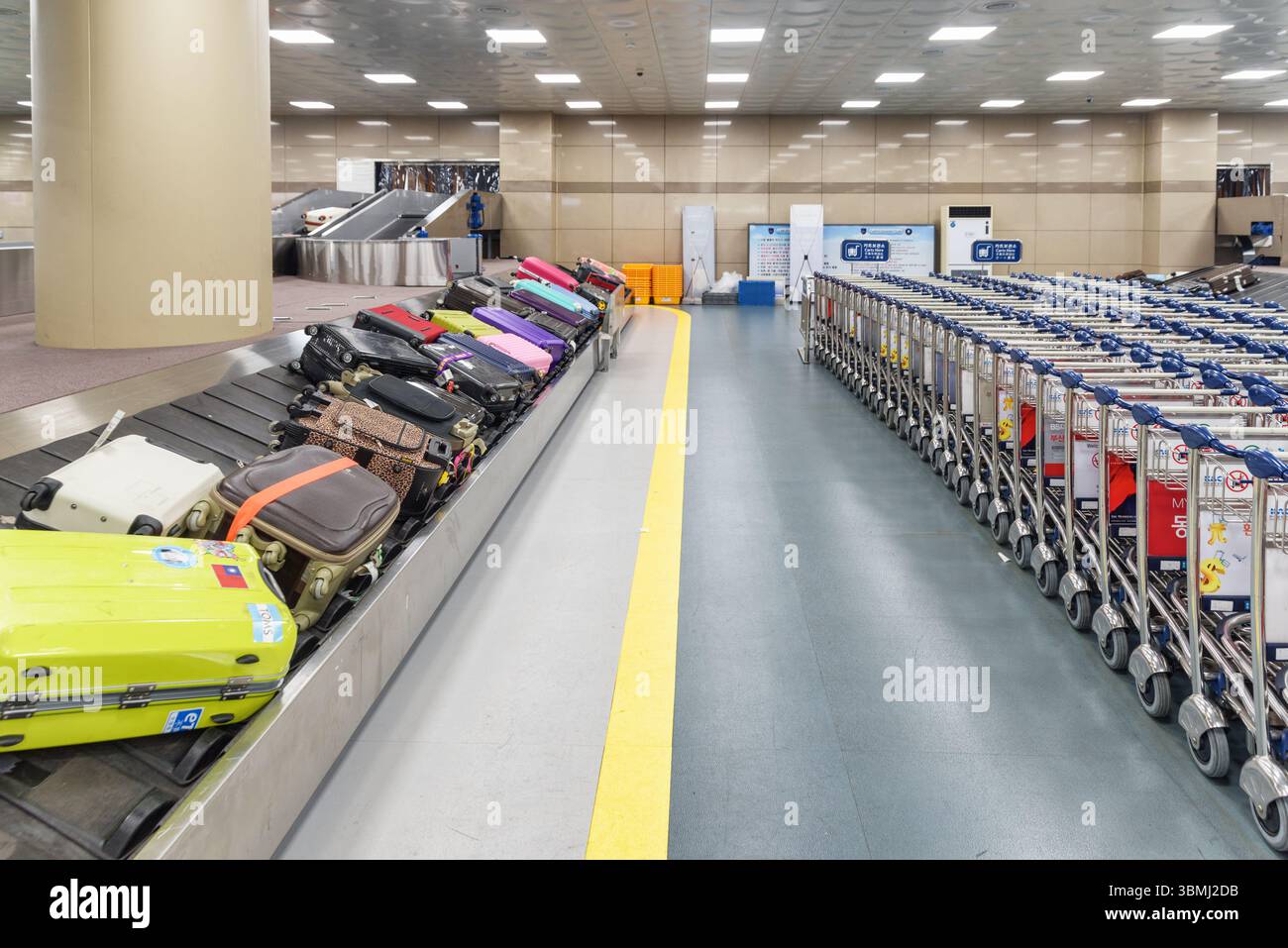 Suitcases on luggage conveyor belt and rows of trolleys, Busan Stock Photo