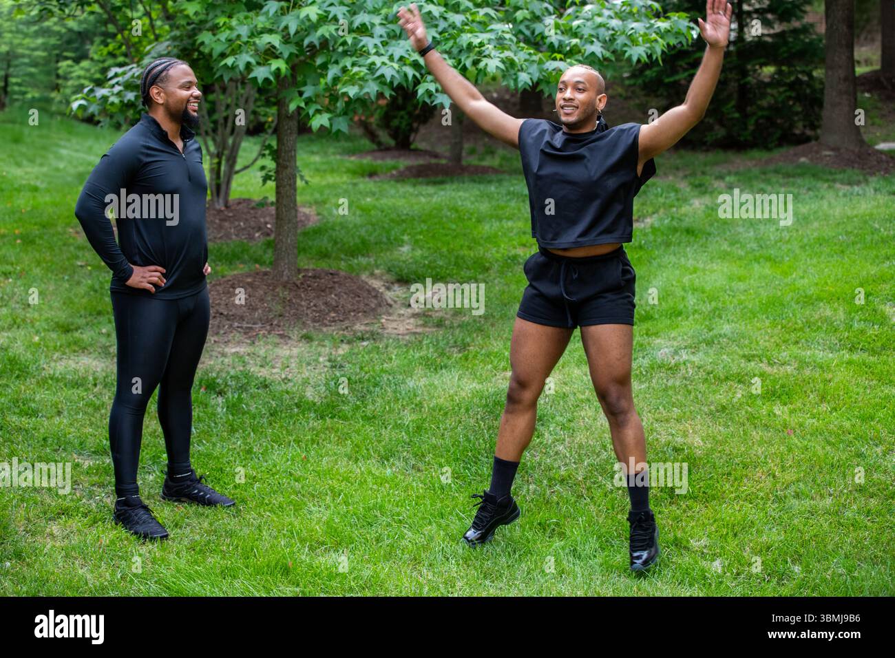 A man doing jumping jacks outdoors under a trainers supervision Stock Photo