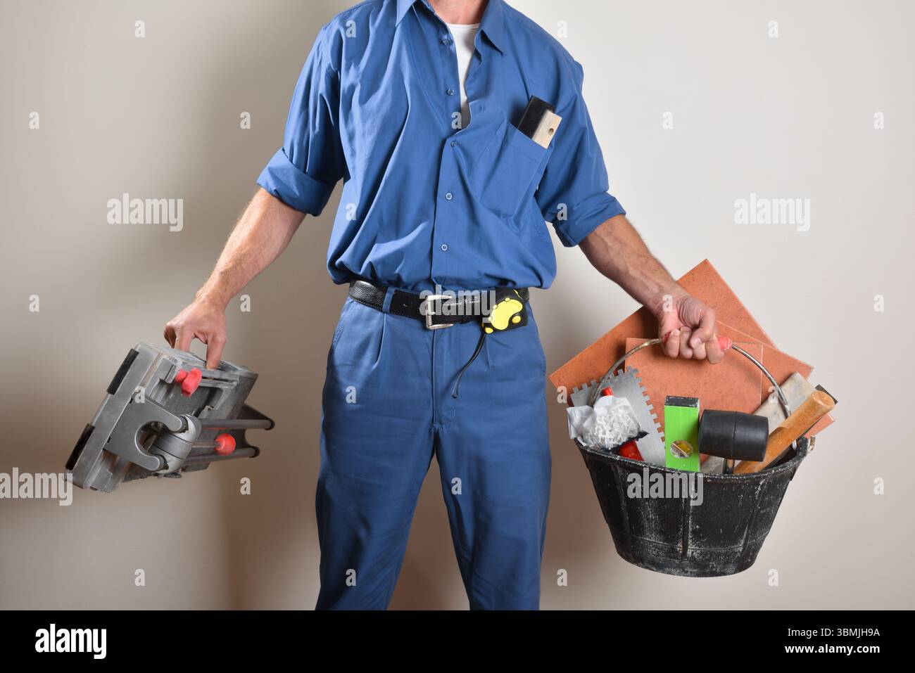 Smiling tiler with ok gesture showing tools and materials on wooden table. Front view. Stock Photo