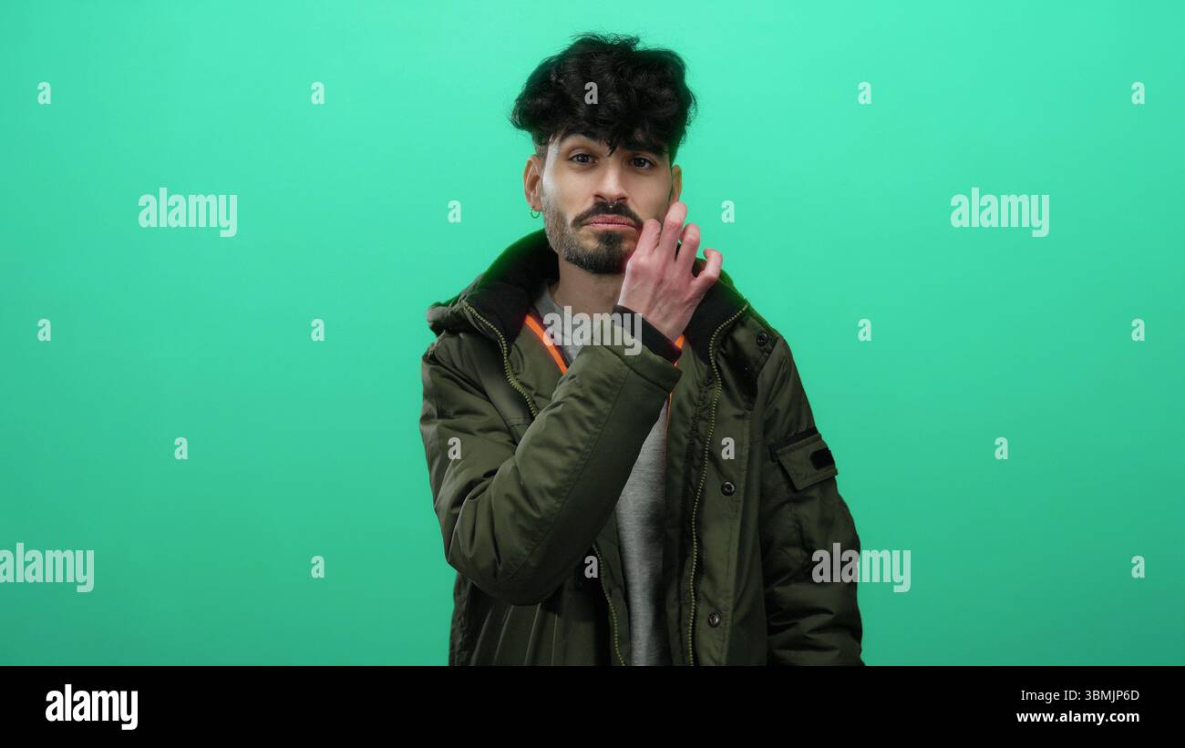 Secretively Young man making a secretive gesture against an isolated green ...