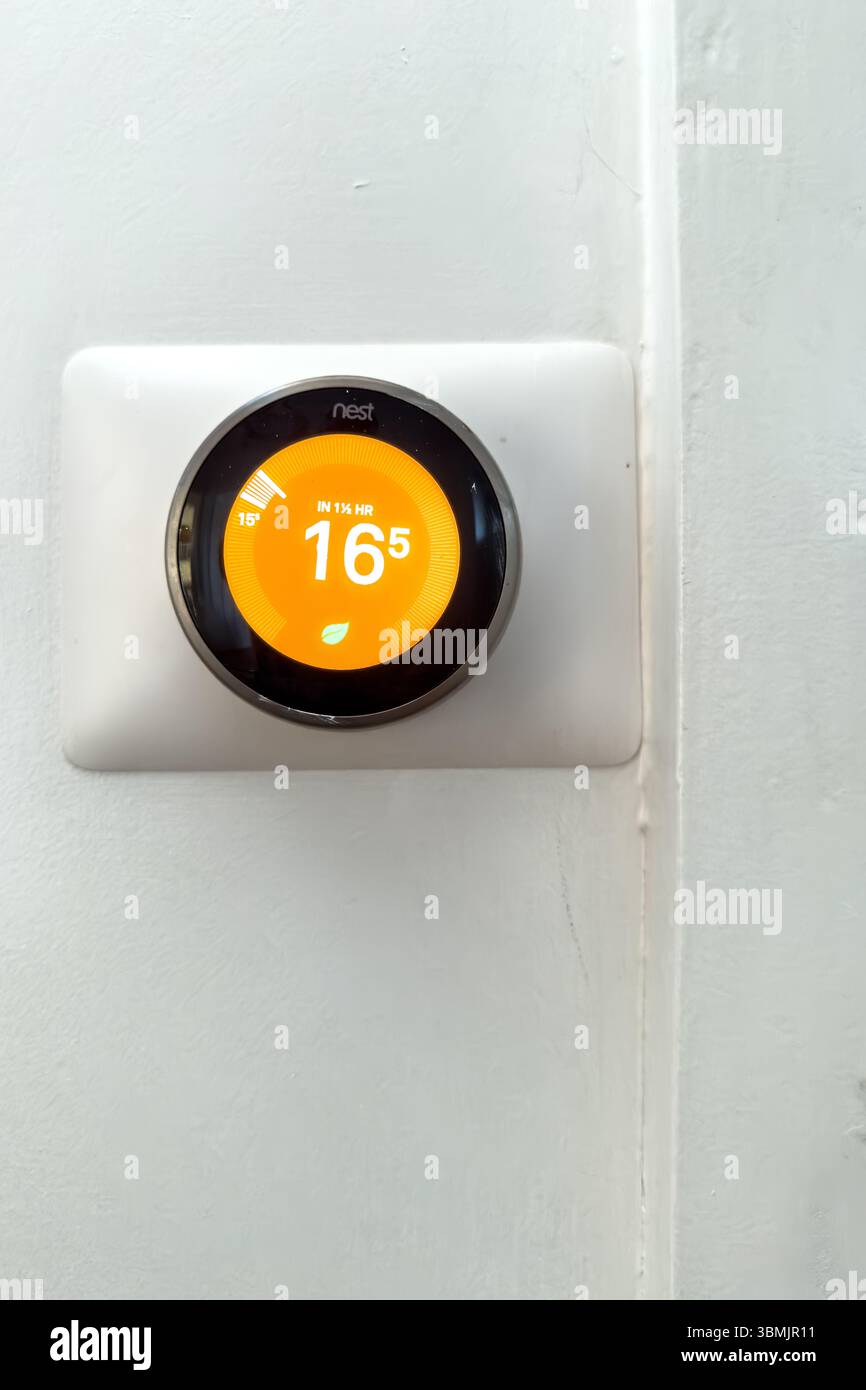 A Nest smart home thermostat mounted on a white wall displaying the temperature set to 16.5 degrees Celsius - heating energy bills home technology - Smartphone Captured Stock Image