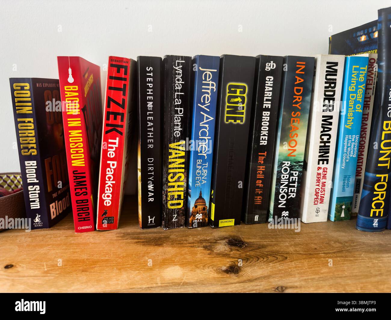 row of crime mystery and thriller novels books lined up on wooden shelf  various covers & titles , stephen leather, peter robinson, jeffrey archer - Smartphone Captured Stock Image