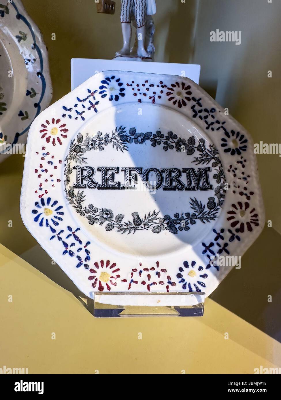 Decorative ceramic plate with floral and text design featuring the word 'REFORM' displayed on a stand with a soft light backdrop - Smartphone Captured Stock Image