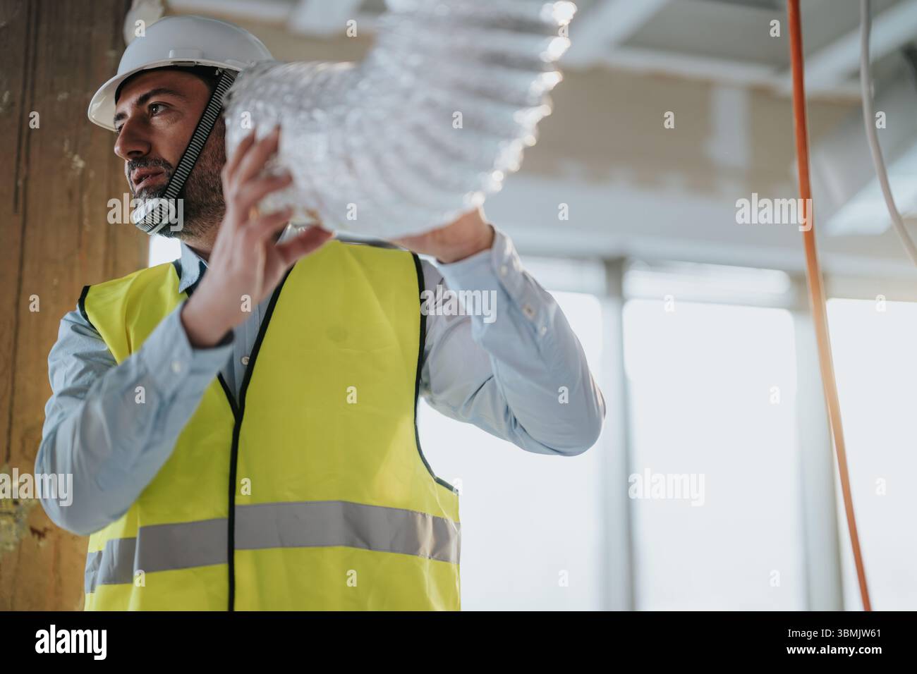 Construction worker adjusting ventilation duct in industrial building ...