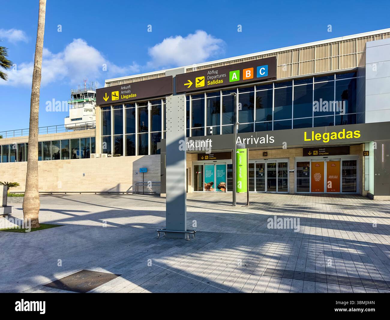 Exterior view of modern tenerife airport arrivals terminal showing entrance and exit signs in multiple languages under a clear blue sky - Smartphone Captured Stock Image