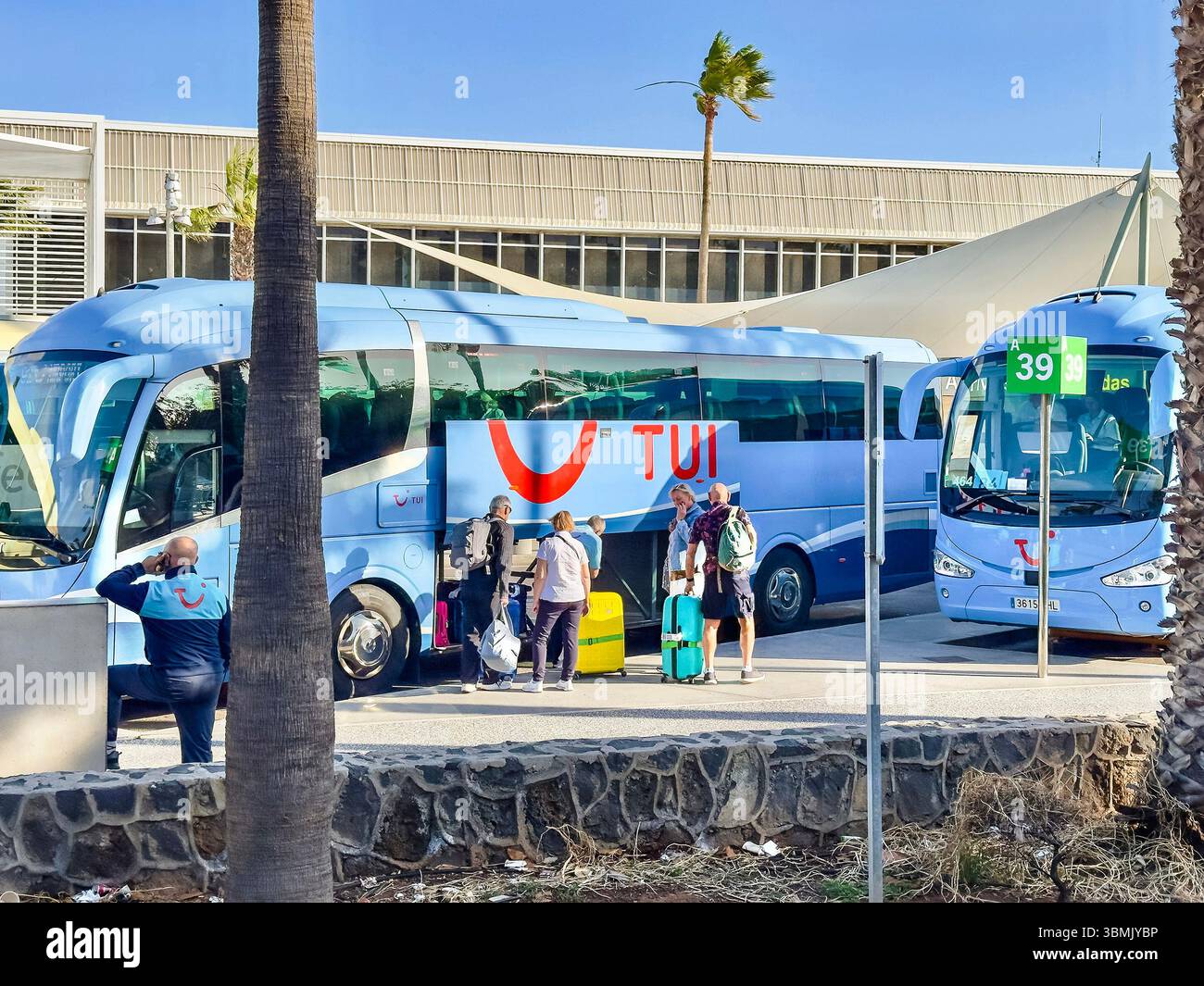 Travelers & luggage  near blue TUI tour buses at tenerife-sur airport, arrivals sign, spain, delays, arrivals, flights,air travel, canary islands - Smartphone Captured Stock Image