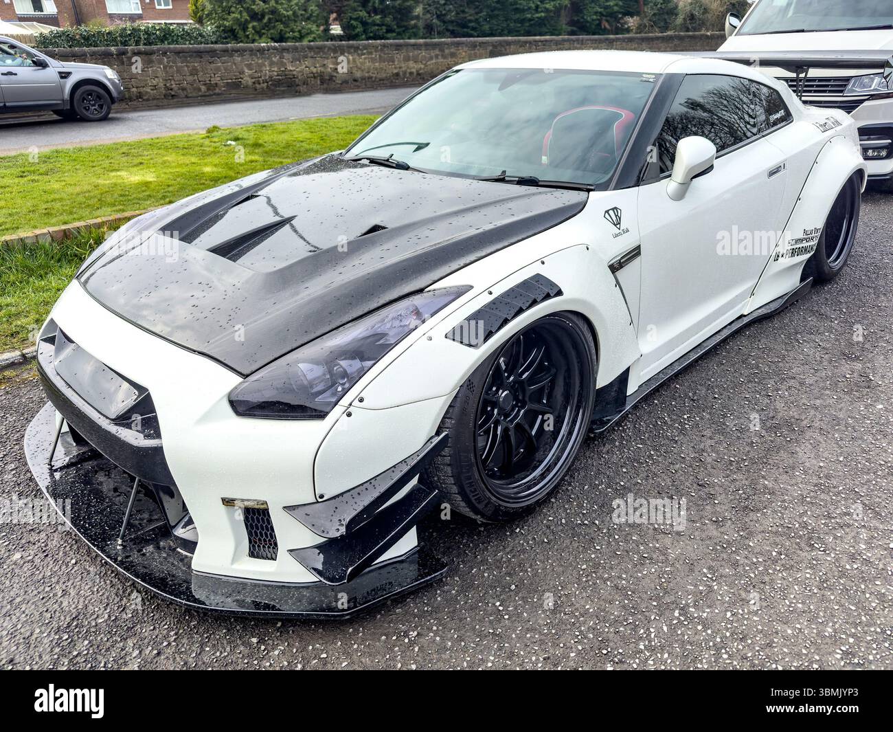 White works nissan GTR sports car with a black hood parked on a wet street, featuring a custom body kit and sleek design elements - Smartphone Captured Stock Image