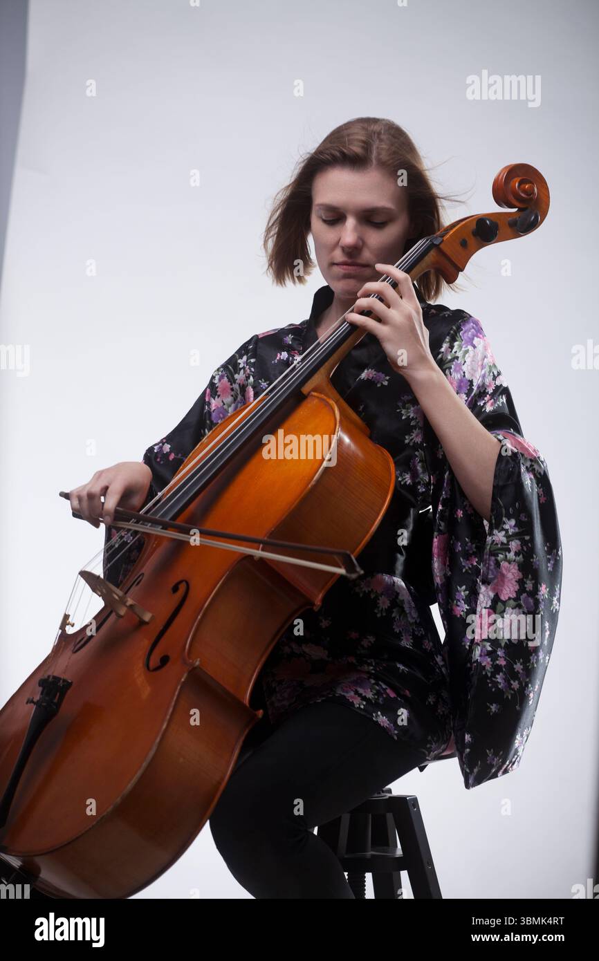 Young adult Caucasian woman in black floral robe playing cello in ...