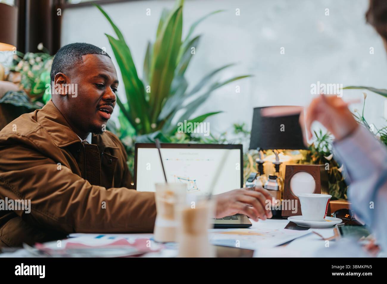 Two Multiracial Professionals Collaborating in a Cafe and Discussing Strategy Stock Photo