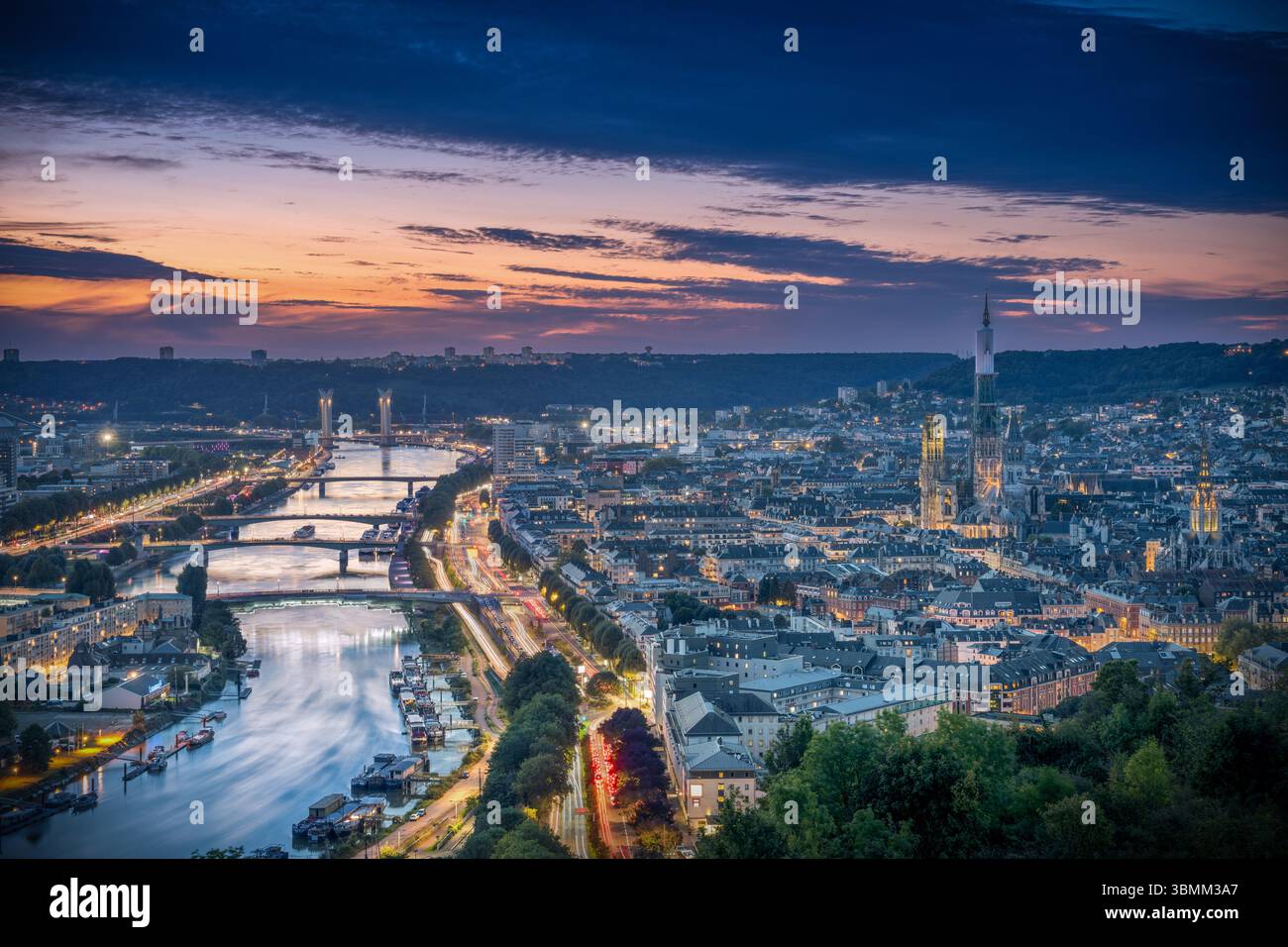 A panoramic view of Rouen, France, from La Côte Sainte-Catherine at sunset. The sky is painted with warm evening colors, city lights begin to glow, an Stock Photo