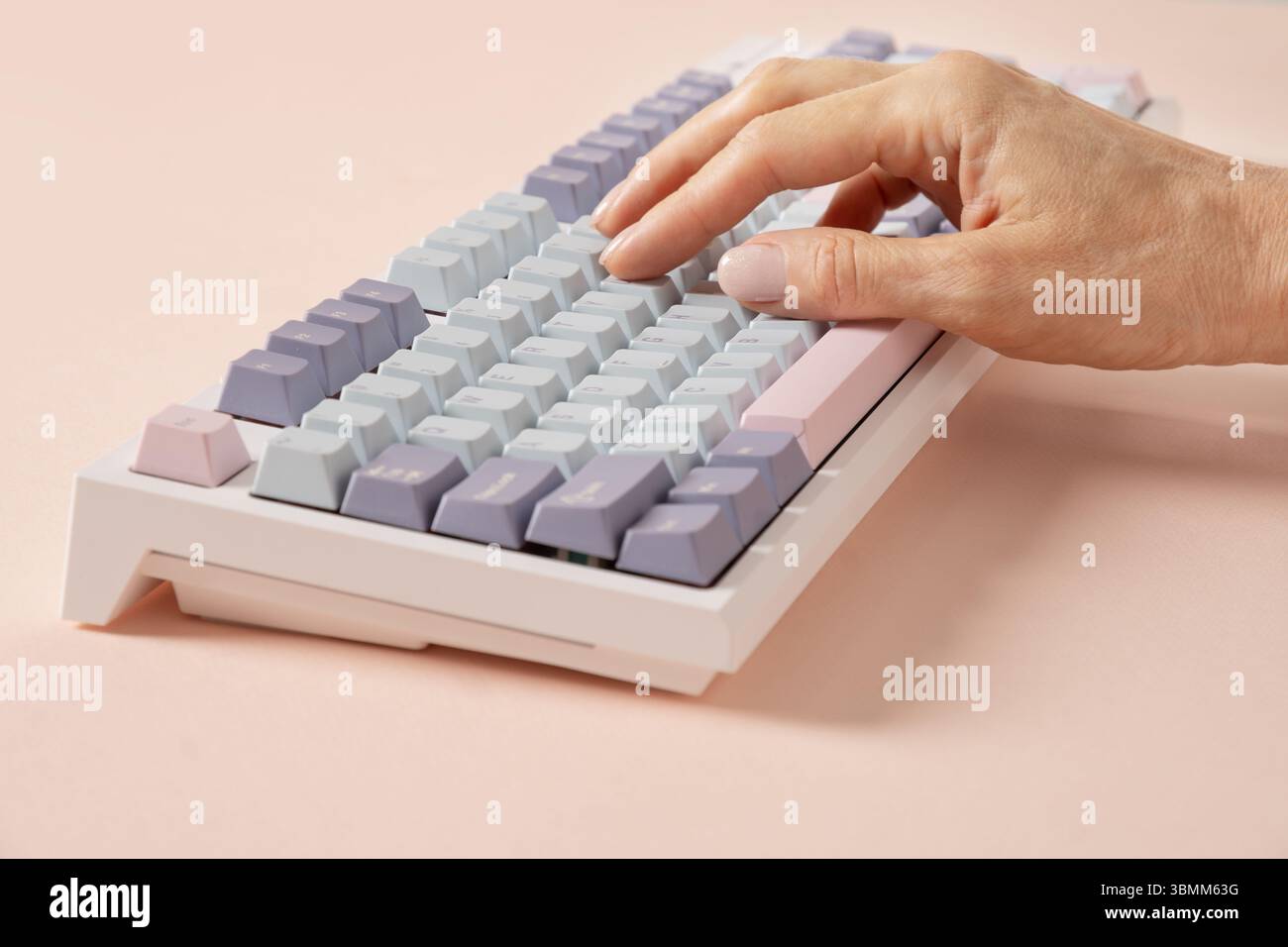 Womans hand typing on mechanical keyboard on pink background. Close up. Stock Photo