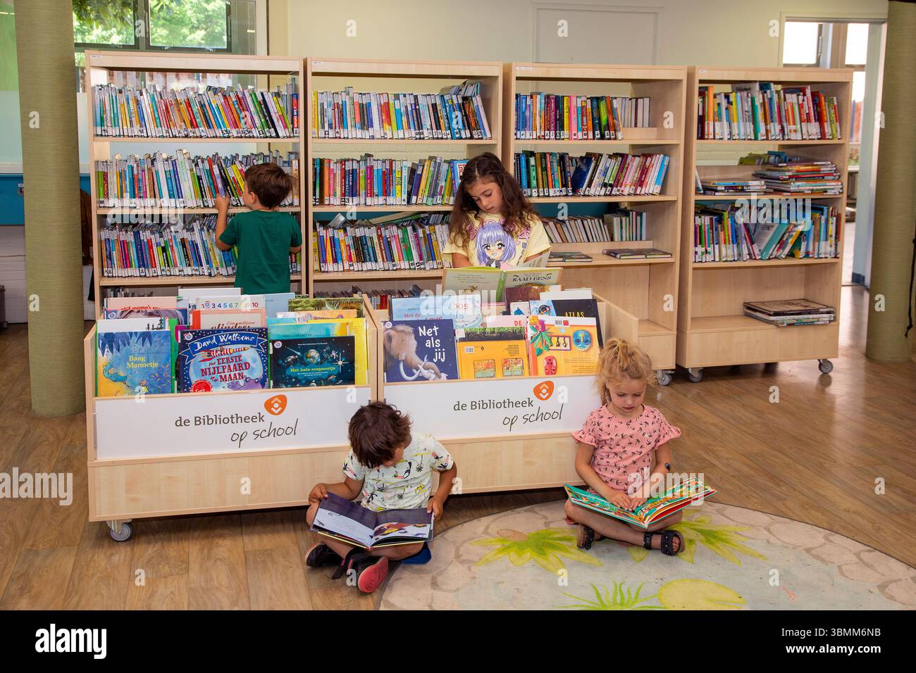 School children reading books on floor in library Stock Photo - Alamy