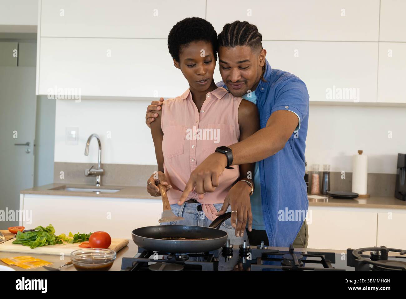 Cooking African American couple stirring food on gas stovetop in modern ...