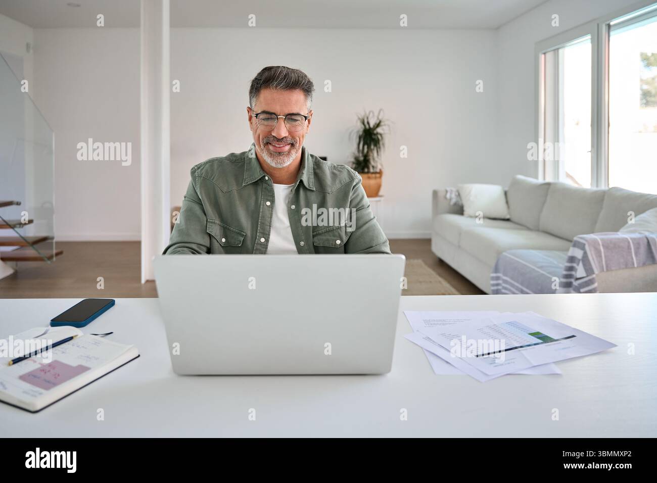 Happy older middle aged man using laptop computer at home table. Stock Photo