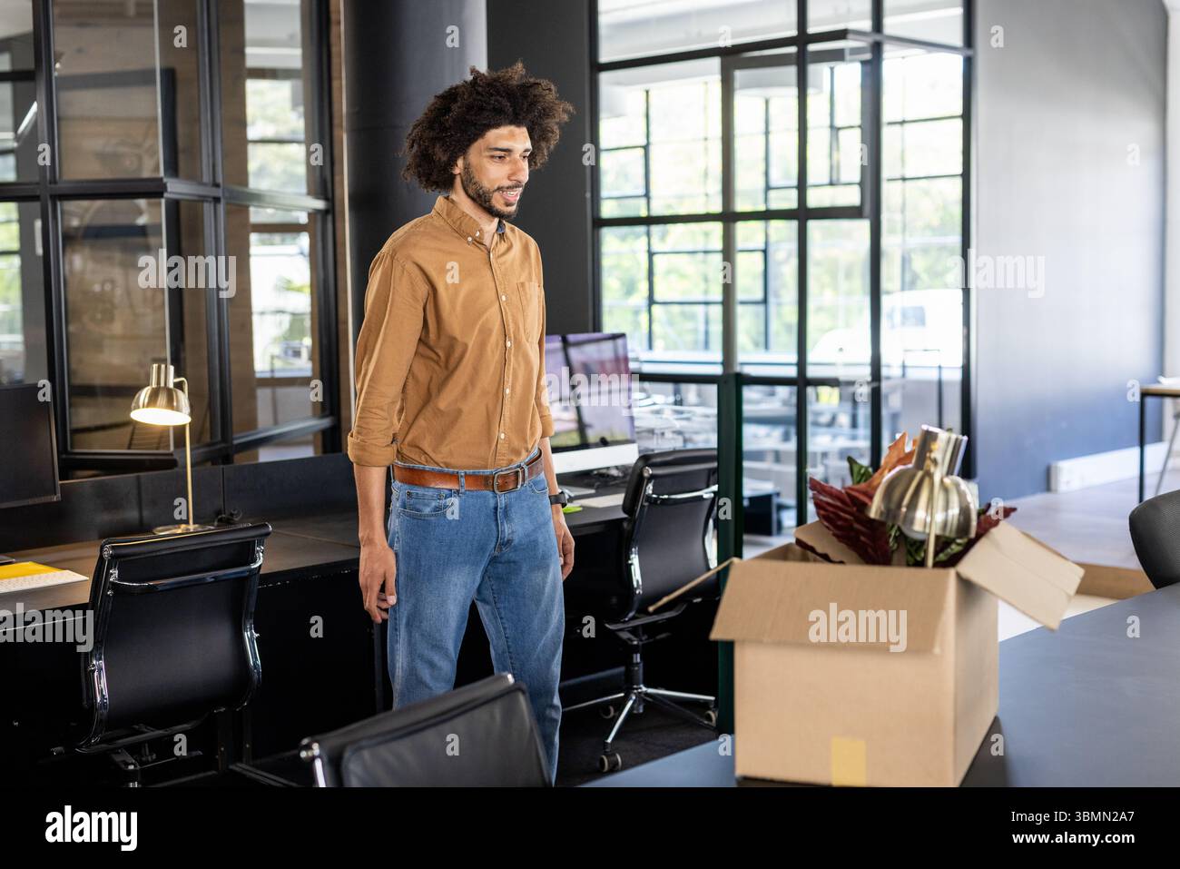 Man standing at workstation in open-plan office unpacking box with lamp and plant, copy space Stock Photo