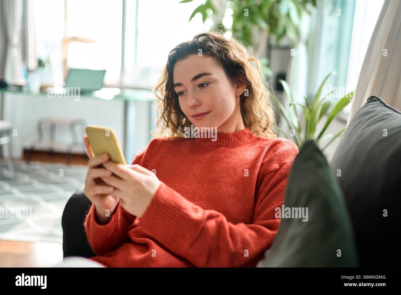 Relaxed young woman sitting on couch using mobile phone technology. Stock Photo