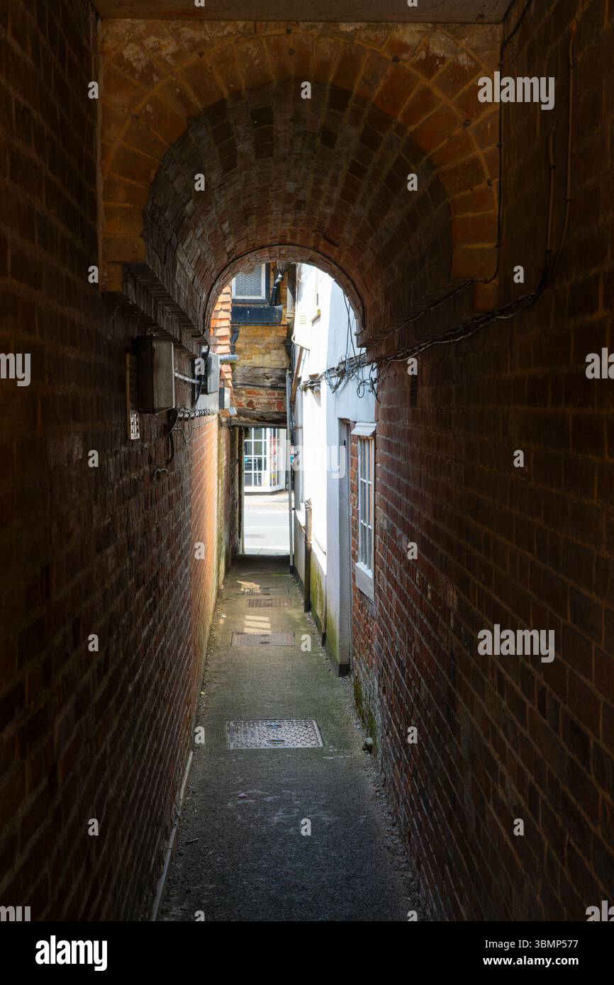 Narrow brick alleyway between buildings leading to Odiham High Street, Odiham, Hampshire, England Stock Photo