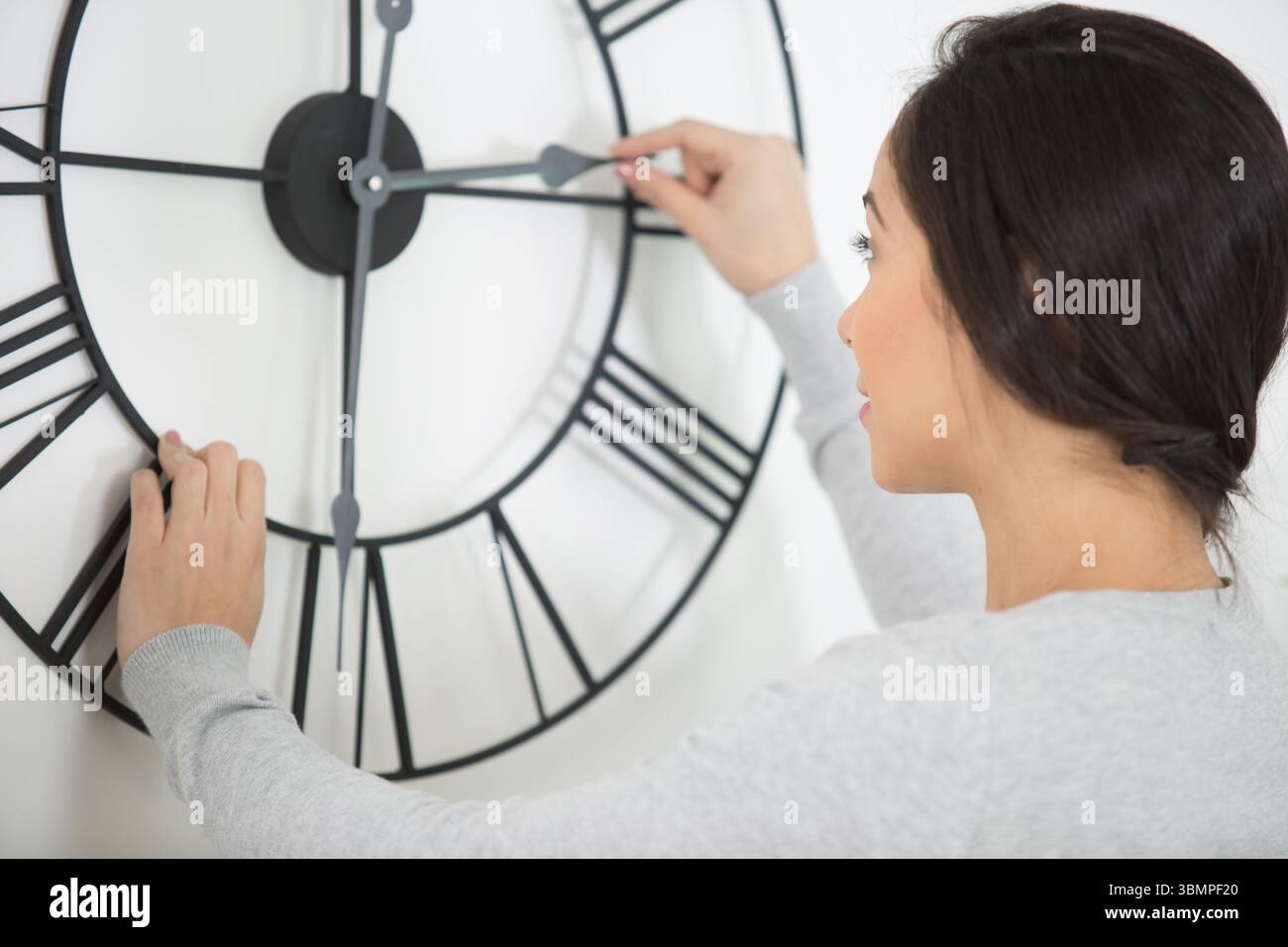 woman setting the time on a wall clock Stock Photo