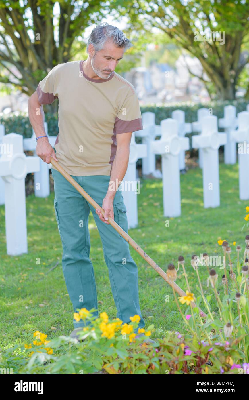 Man hoeing flower beds next to graves Stock Photo