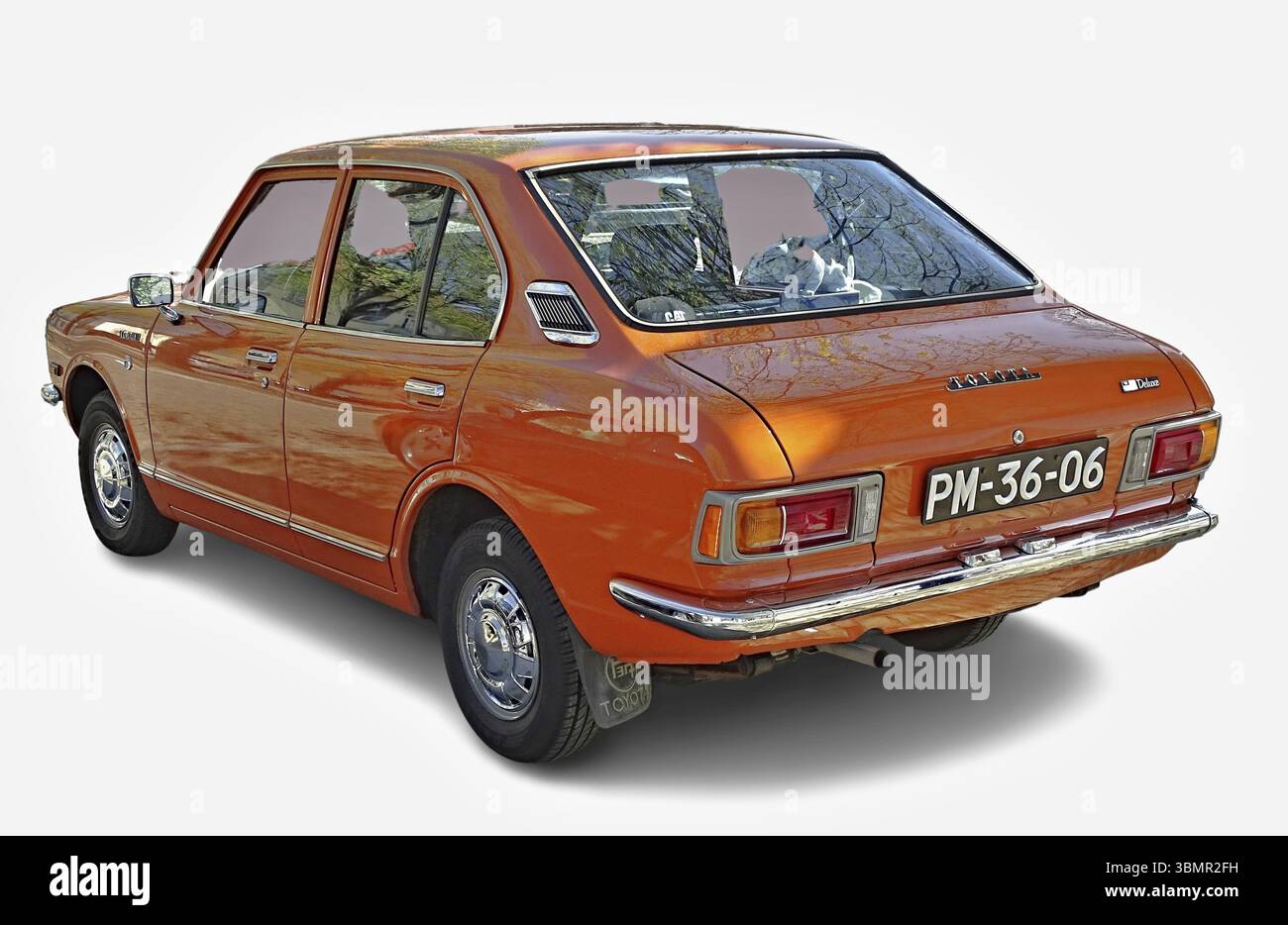 Classic orange Toyota Corolla parked, reflecting trees in the back window, showcasing its vintage charm Stock Photo