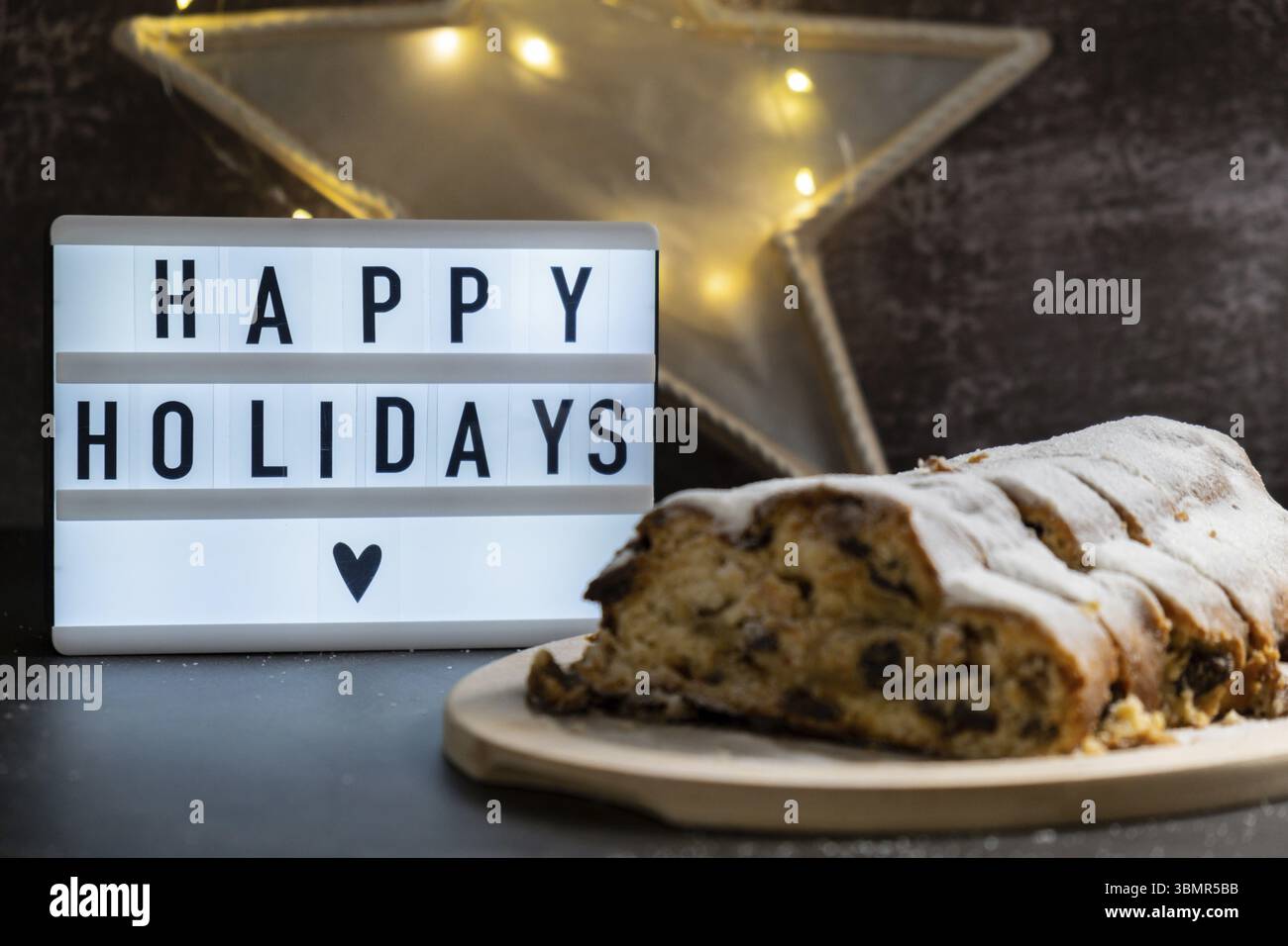 Lightbox with text HAPPY HOLIDAYS. Traditional German Christmas stollen cake in background of handmade festive decor. Winter holiday treats. Vegan bak Stock Photo