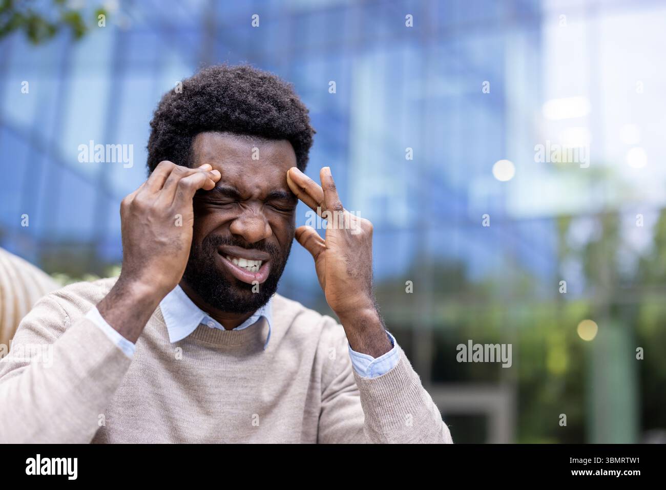 A man experiencing a headache, pressing his fingers to his temples with eyes closed outdoors. Stock Photo