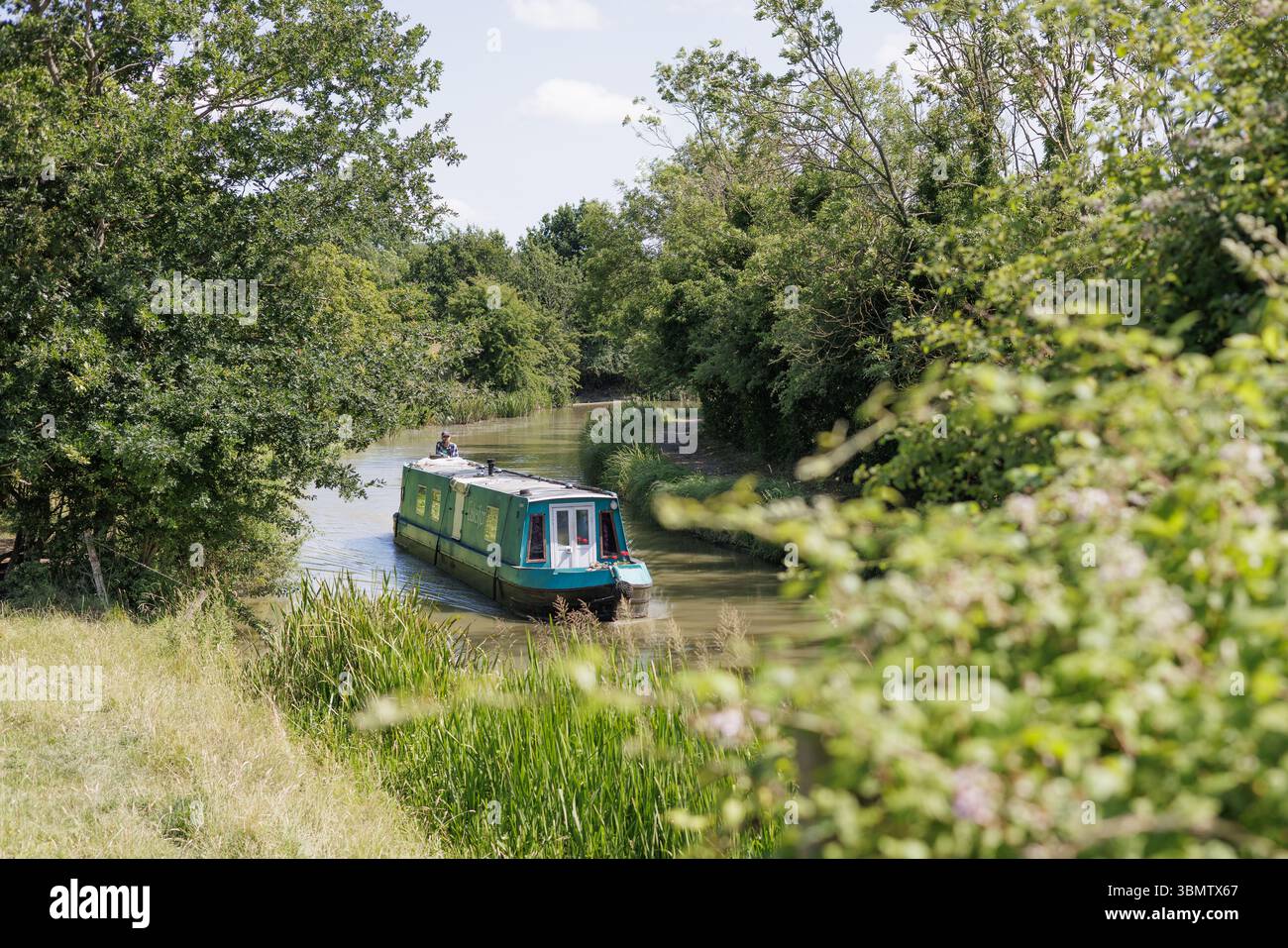Crick, Northamptonshire, UK: A narrowboat is steered around a bend on a stretch of the Grand Union Canal that passes through rural Northamptonsire. Stock Photo