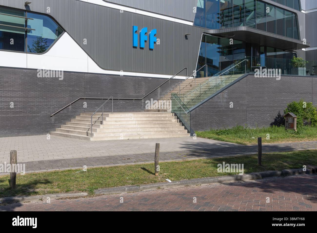 Modern office building with the blue IFF logo (International Flavors Fragrances) prominently displayed near the entrance with stairs and greenery. Oeg Stock Photo