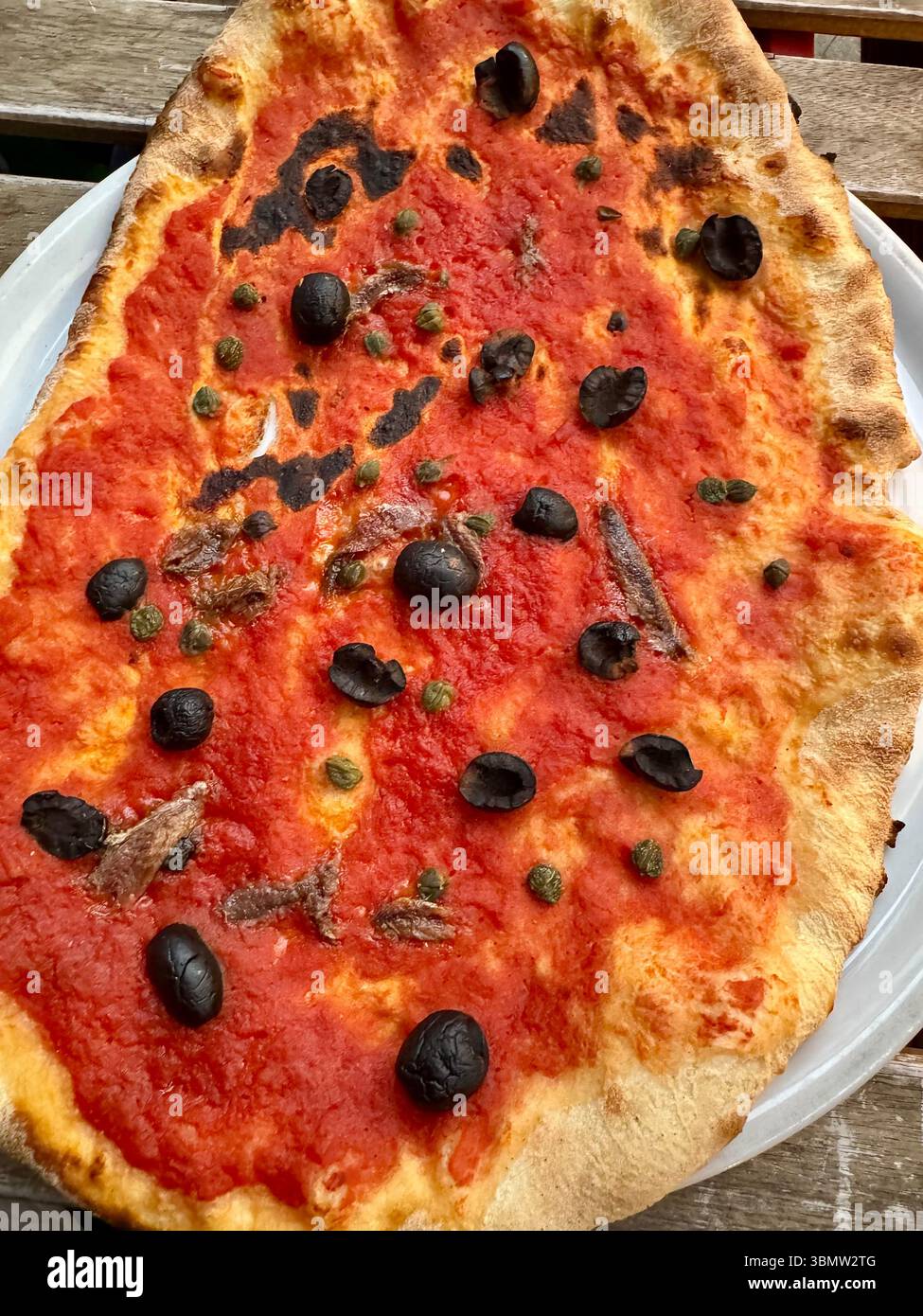 Close-up of a Traditional Italian pizza topped with tomato sauce, anchovies, black olives, and capers on a thin crust served on a white plate. - Smartphone Captured Stock Image