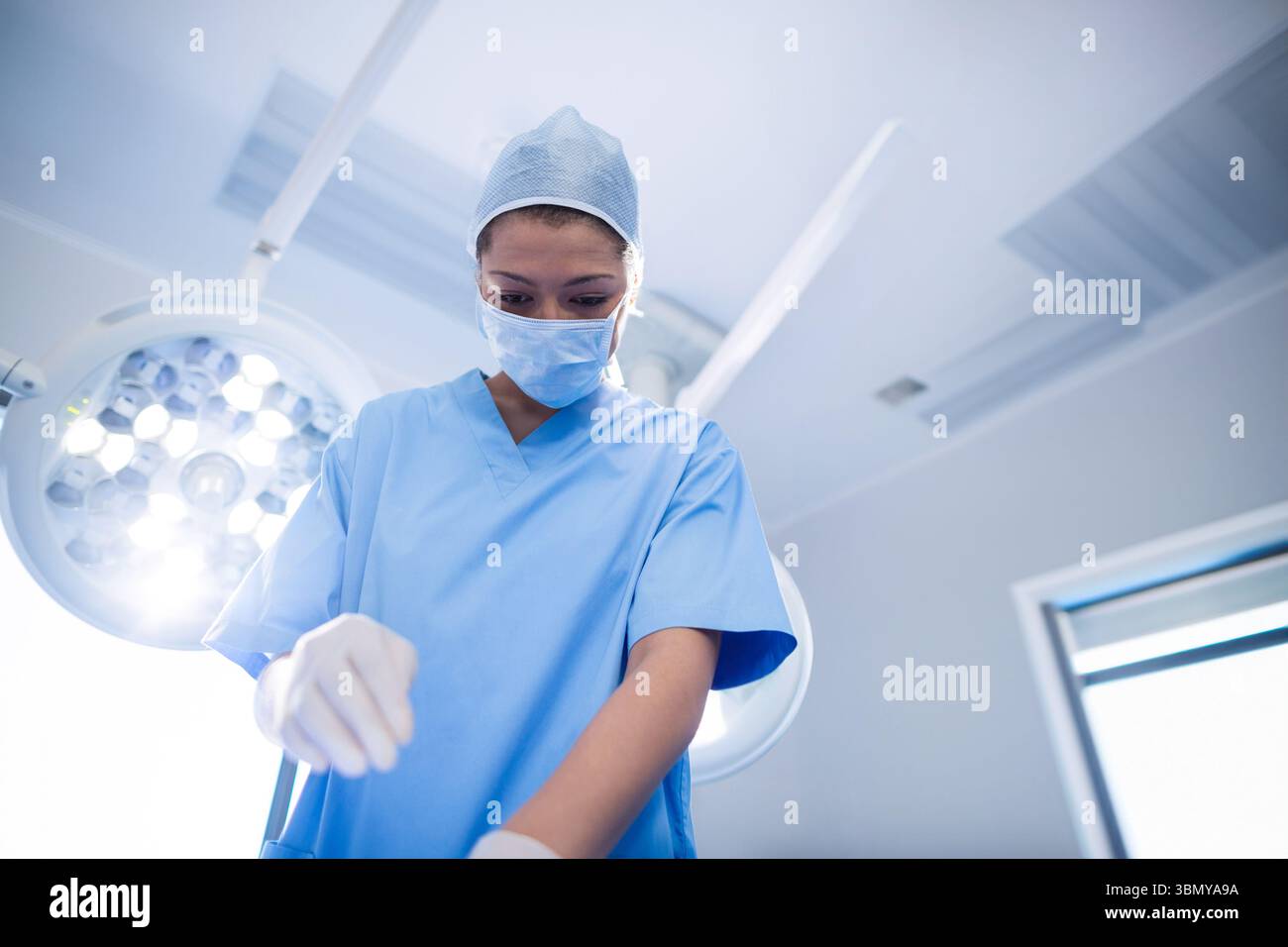 Female surgeon in blue scrubs leaning under surgical lights in ...