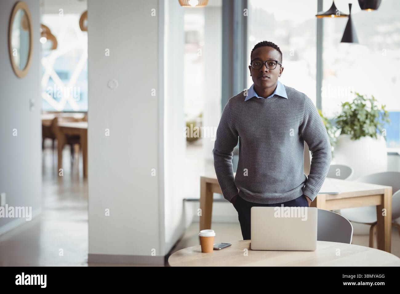 African American man wearing business attire working on laptop in cafe with coffee cup, smartphone Stock Photo