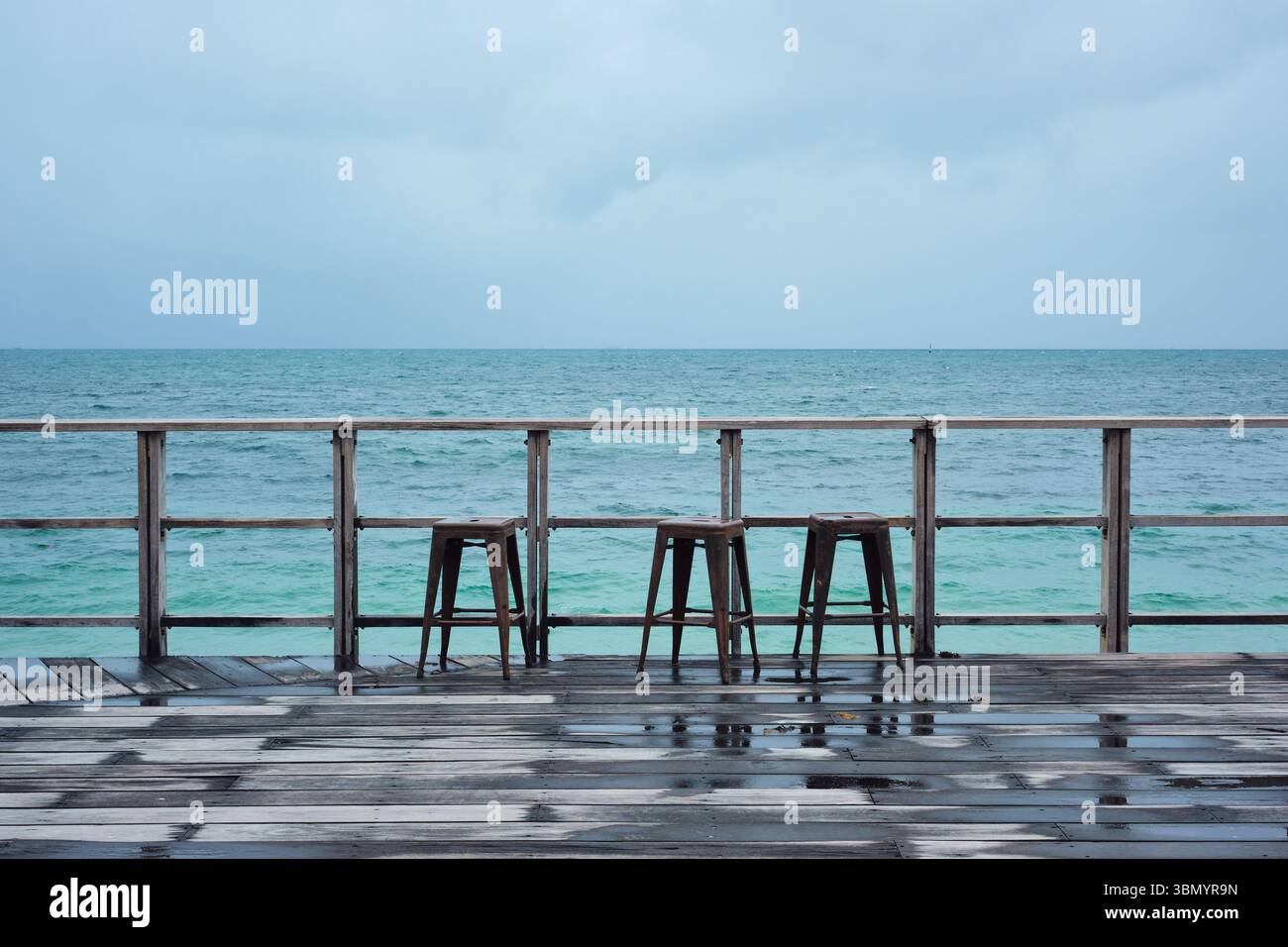 Three stools on a wooden platform on a grey, wet, moody winter day by the sea at Bather's Beach, Fremantle, Perth, Western Australia. Stock Photo