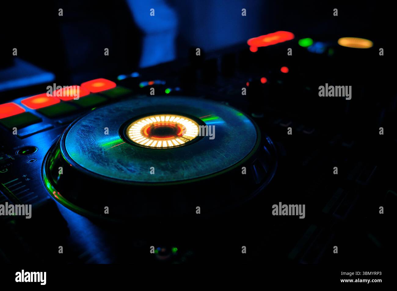 Close-up of DJ mixer with glowing lights in dark club setting Stock Photo
