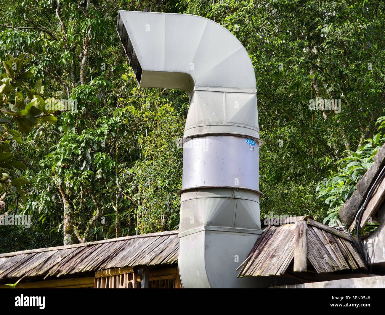 A curved industrial exhaust vent made of metal, attached to the roof of a building with a bamboo structure Stock Photo