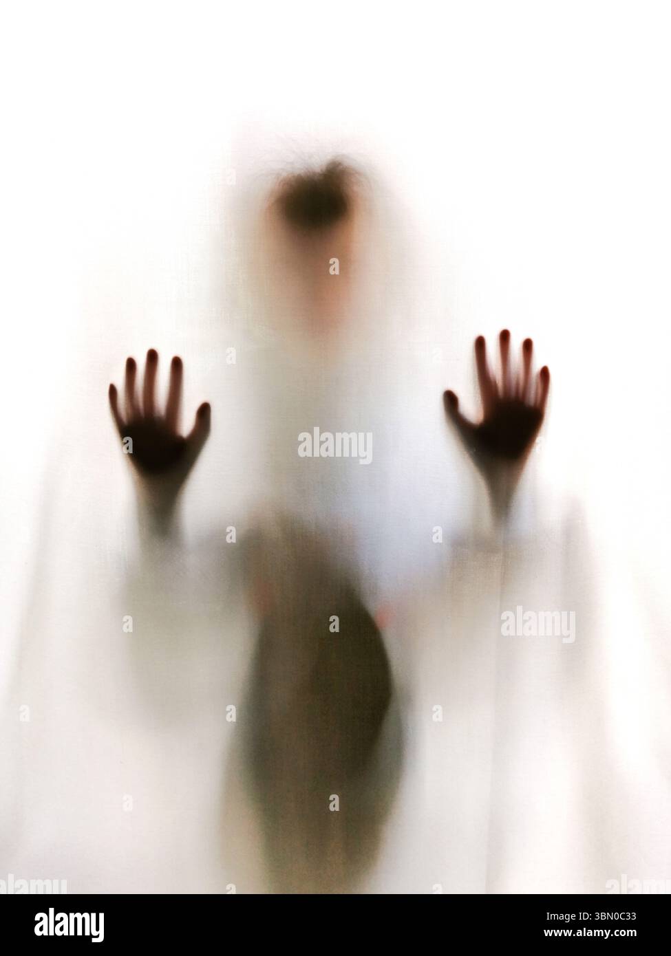 A figure stands behind frosted glass, pressing their hands against it. The light filters through, creating a blurred and abstract appearance - Smartphone Captured Stock Image