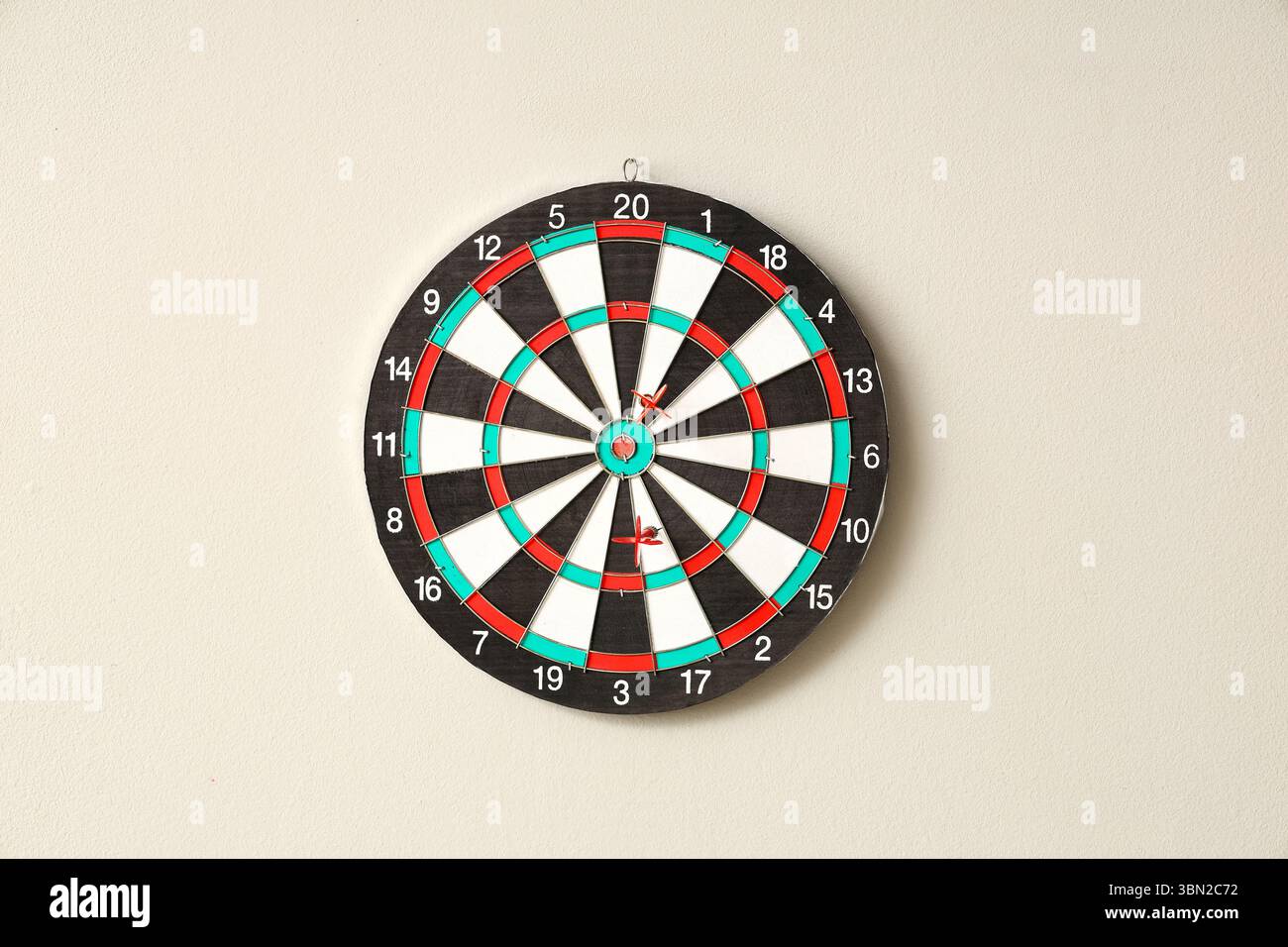 Board with darts hanging on light wall Stock Photo