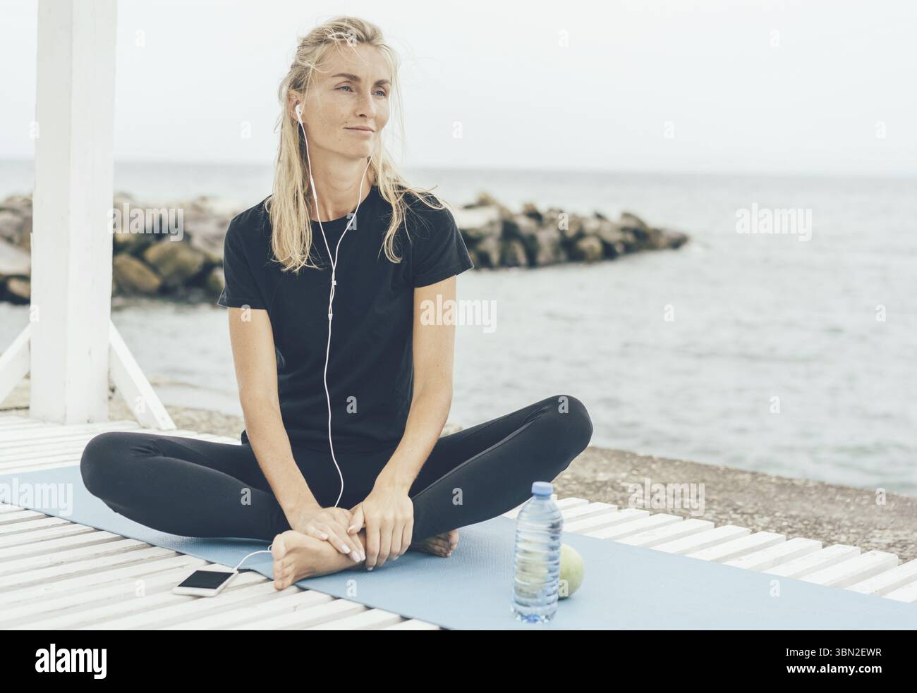 Frau nach dem Sporttraining draussen ausruhen und Musik oder Meditation auf Kopfhoerern hoeren Stock Photo