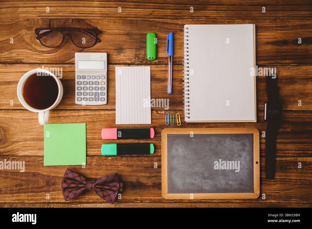 Flat-lay scene showing coffee cup, glasses, calculator, notepad, pen, highlighters on wood table Stock Photo