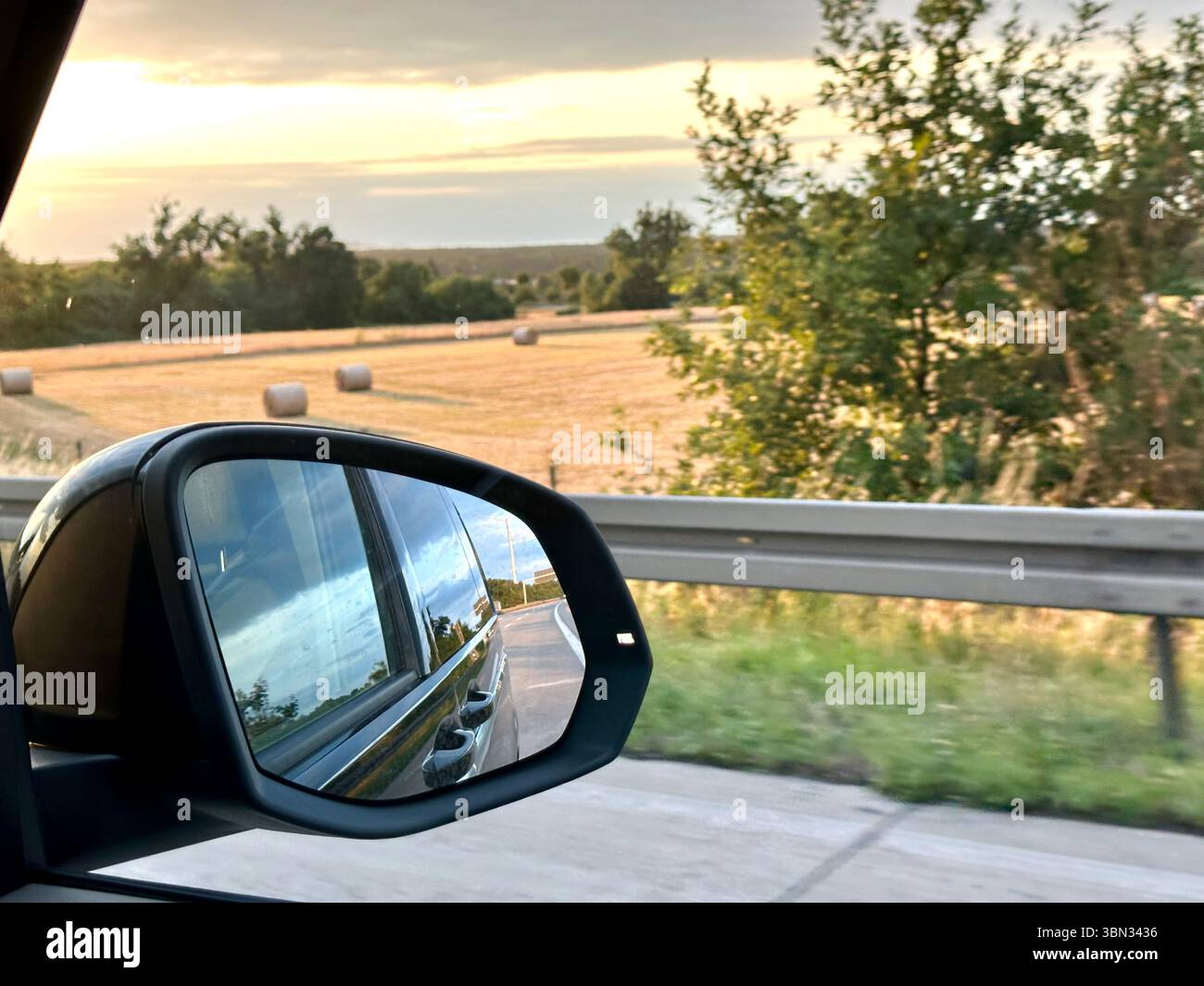 A view from the side-vision mirror of a car on the German autobahn showing the landscape next to the road at sunset - Smartphone Captured Stock Image