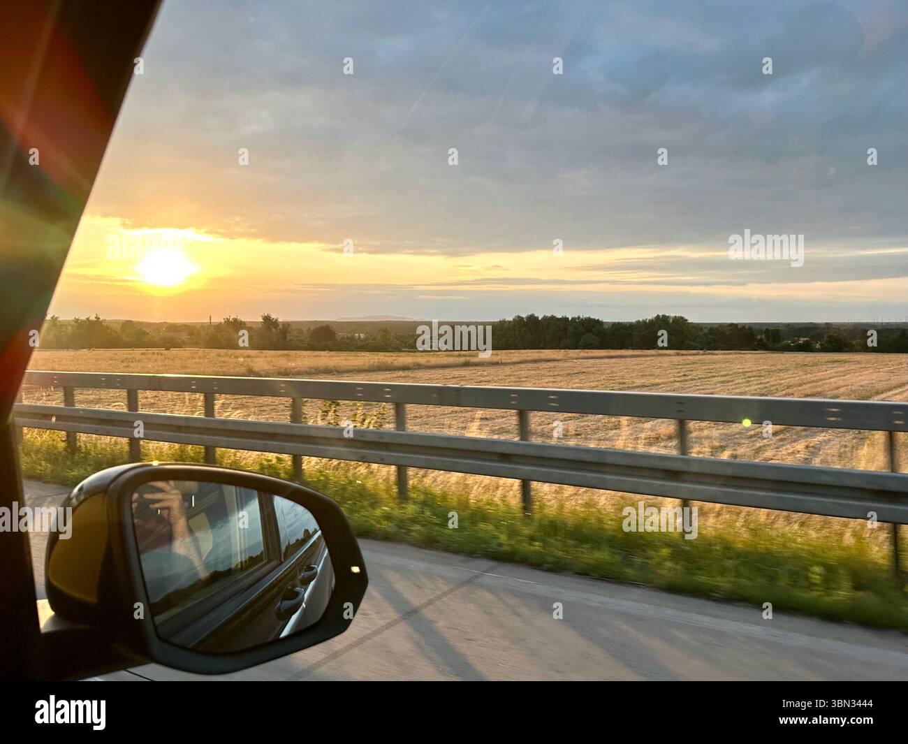 A view from the side-vision mirror of a car on the German autobahn showing the landscape next to the road at sunset - Smartphone Captured Stock Image