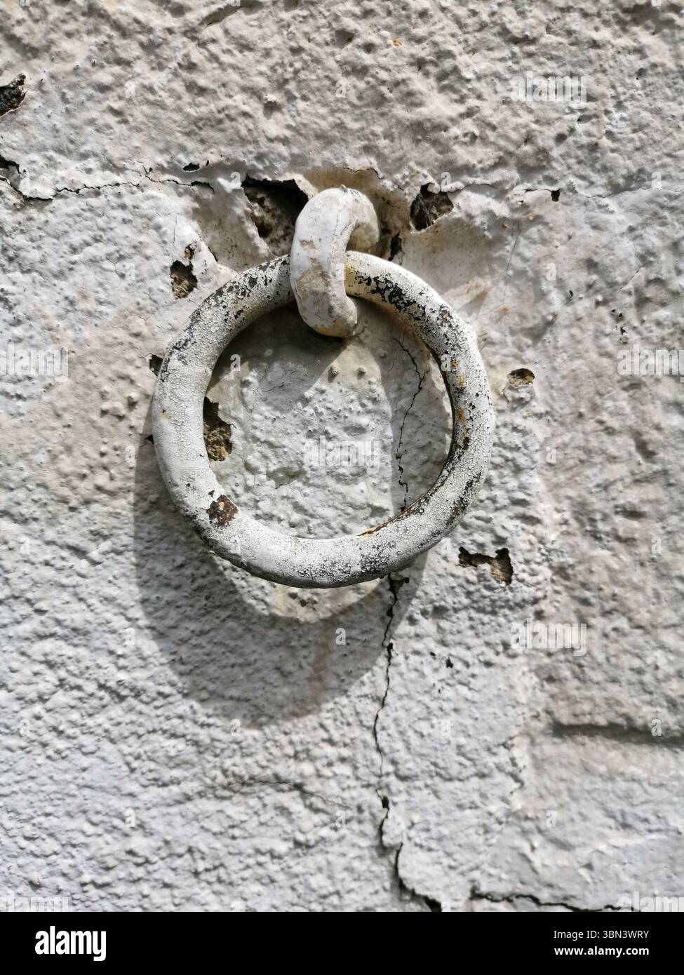 A worn metal ring is fixed to a cracked, peeling wall, highlighting the passage of time - Smartphone Captured Stock Image