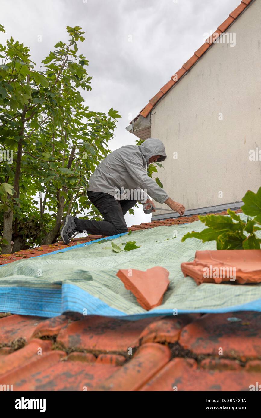 A man places a tarpaulin on a roof after bad weather Stock Photo
