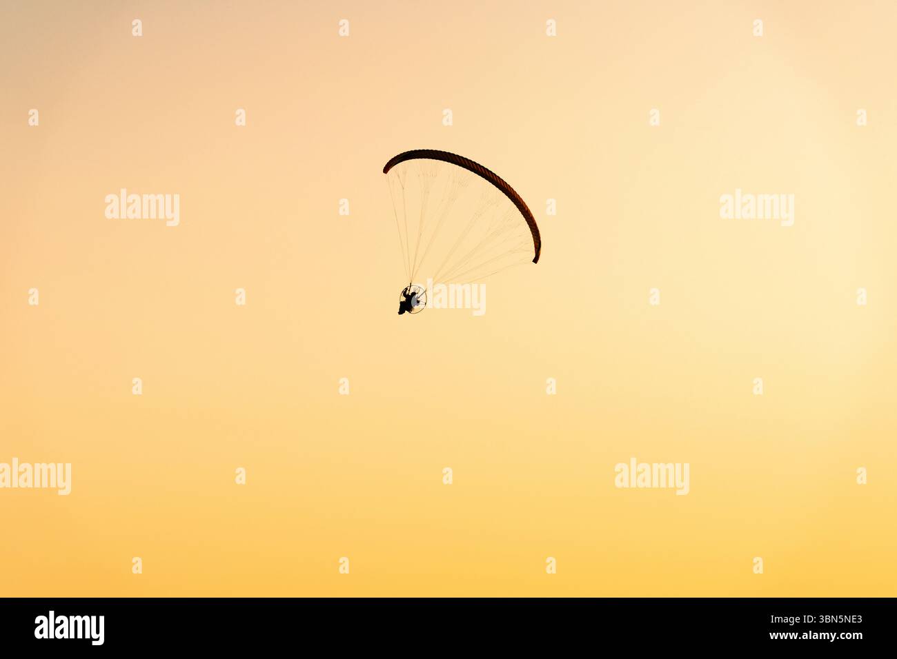 Lone paraglider flying across a brilliant orange and yellow sunrise sky ...