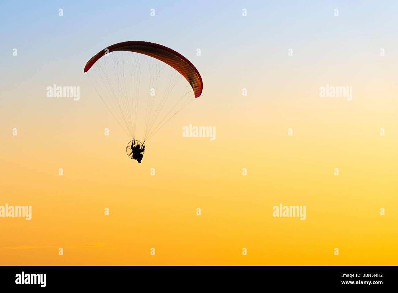 Lone paraglider flying across a brilliant orange and yellow sunrise sky ...