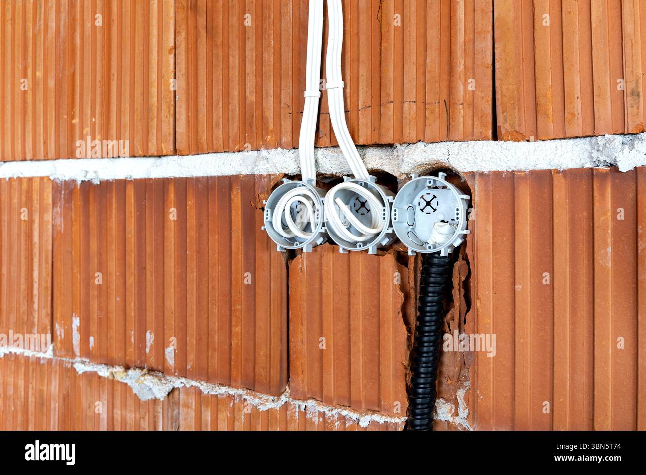 Socket back boxes with wires in a brick wall. New electrical wiring installation Stock Photo