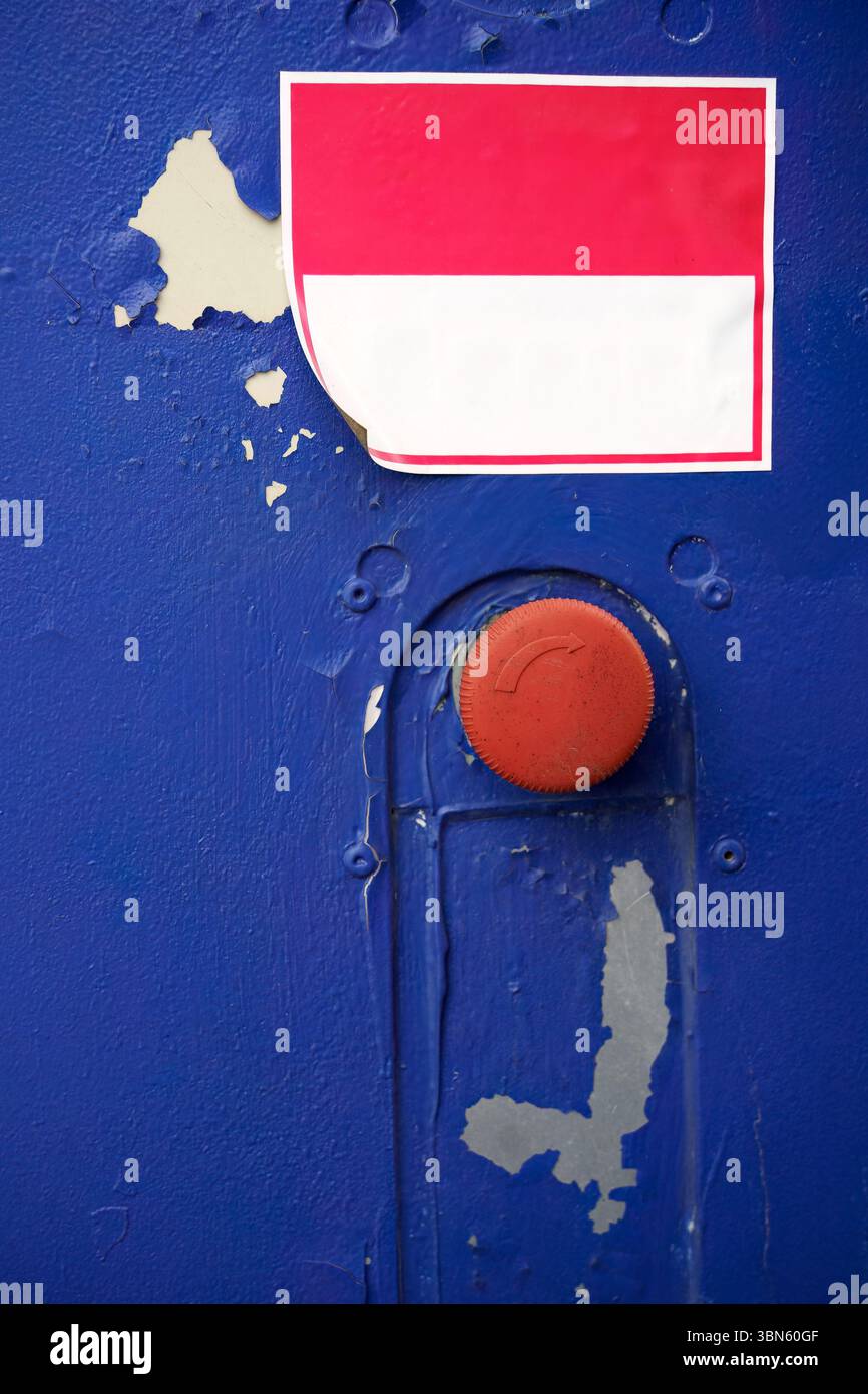Emergency push button with blank red and white sticker on worn blue surface. Stock Photo