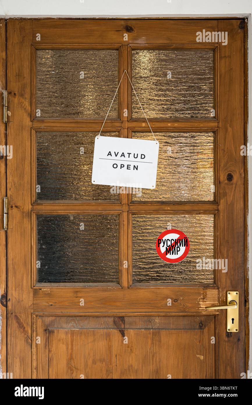 Vintage wooden door with "Open" sign in Estonian and English, and a political sticker rejecting the "Russian World" ideology, Estonia. Stock Photo