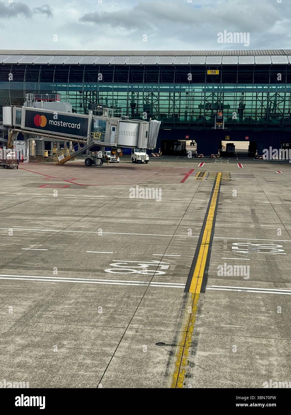 Jet bridge and Mastercard-branded boarding gate at Brussels Airport tarmac under overcast sky. - Smartphone Captured Stock Image