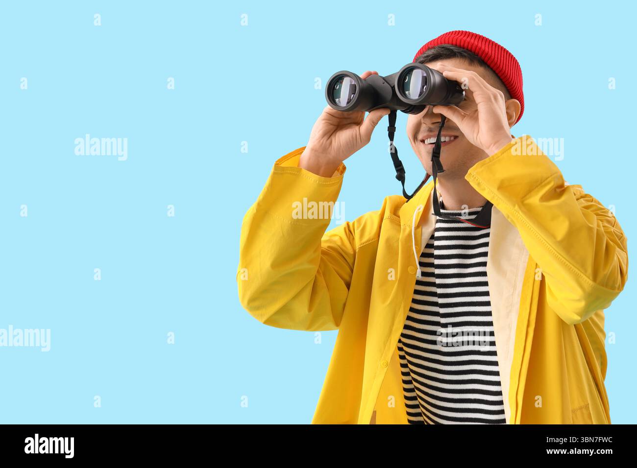 Young sailor looking through binoculars on blue background Stock Photo